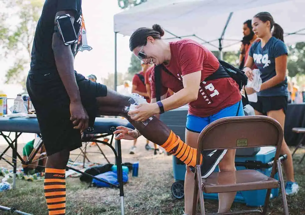 Sports therapist providing injury treatment to athlete at outdoor event.