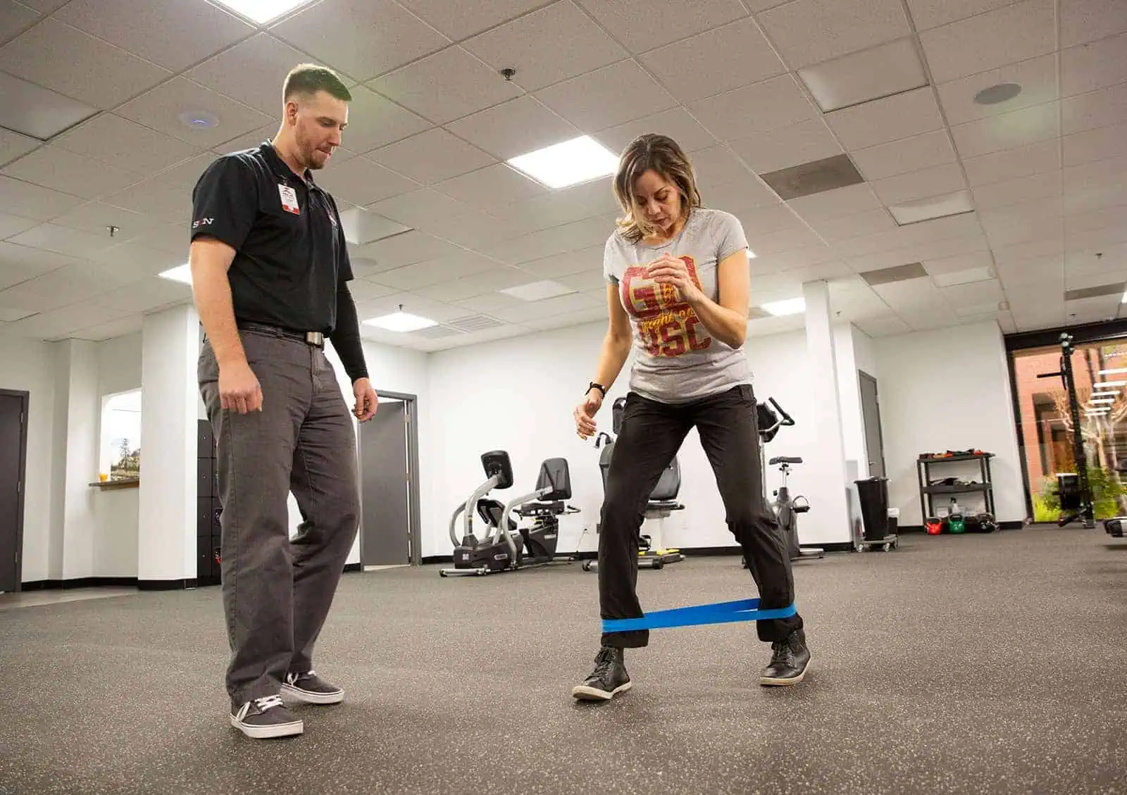 Physical therapist supervising a woman performing resistance band exercise in a clinic.