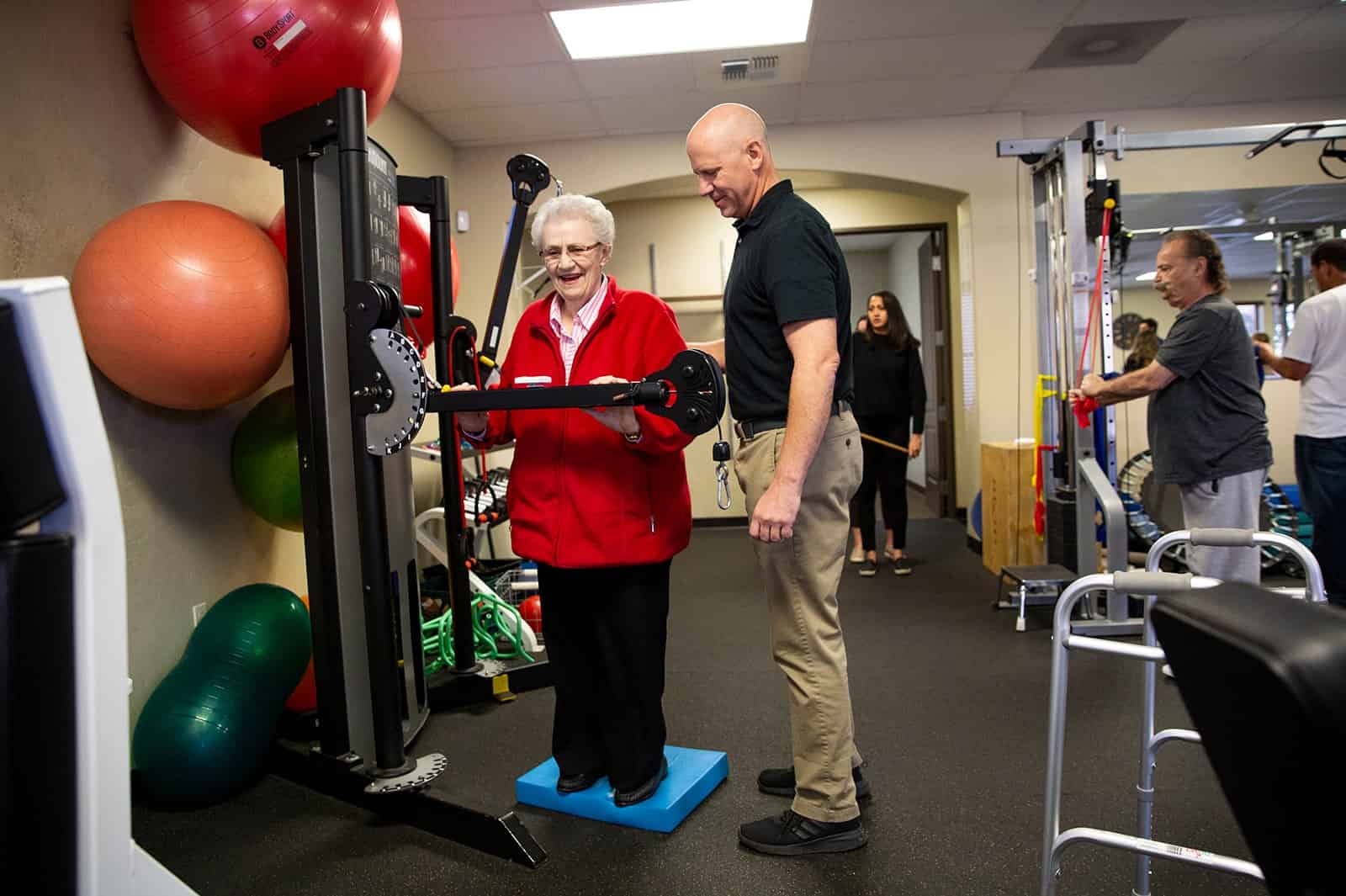 Senior woman doing strength training with trainer at PRO~PT gym.