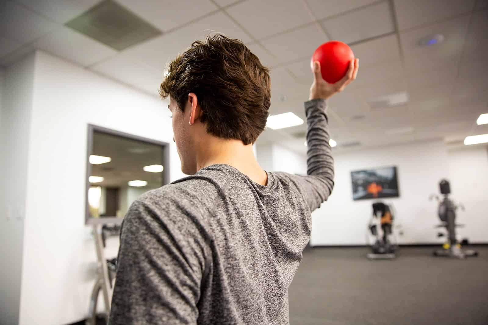 Man performing physical therapy exercises with a red ball in a modern gym.