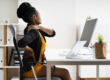 Woman holding her neck and back while sitting in front of her computer at a desk