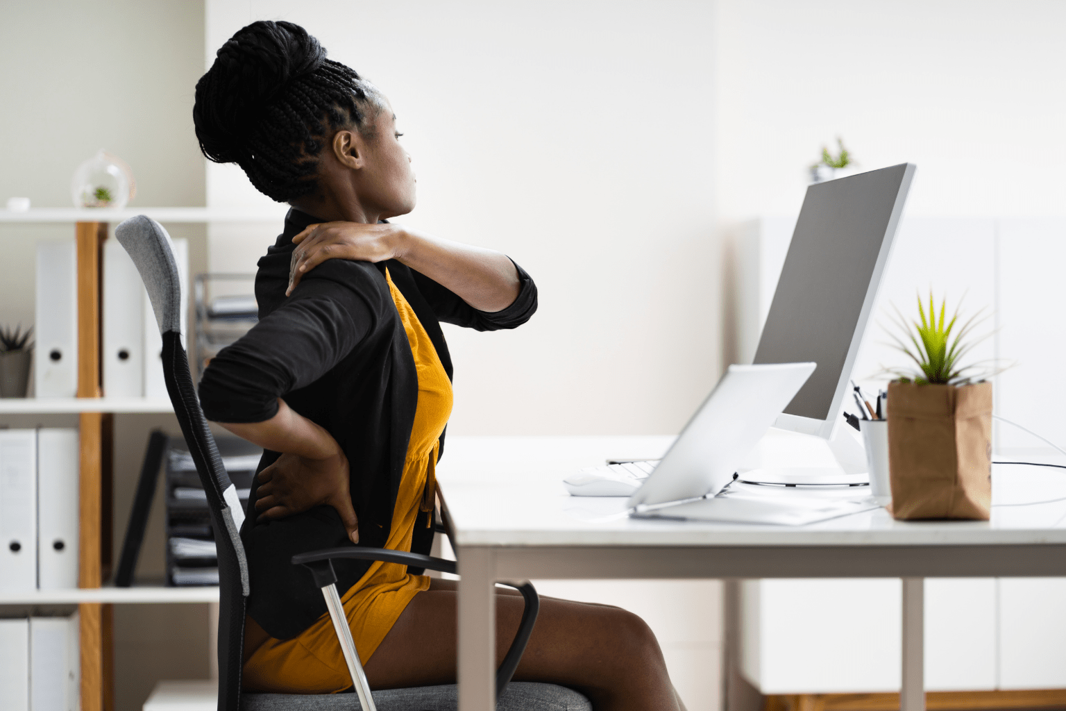 Woman holding her neck and back while sitting in front of her computer at a desk