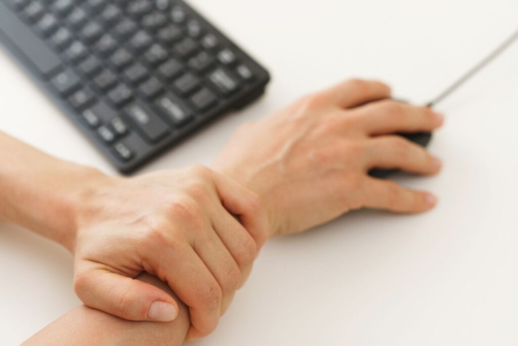Closeup of hands, a person playing video games on the computer and holding their wrist in pain