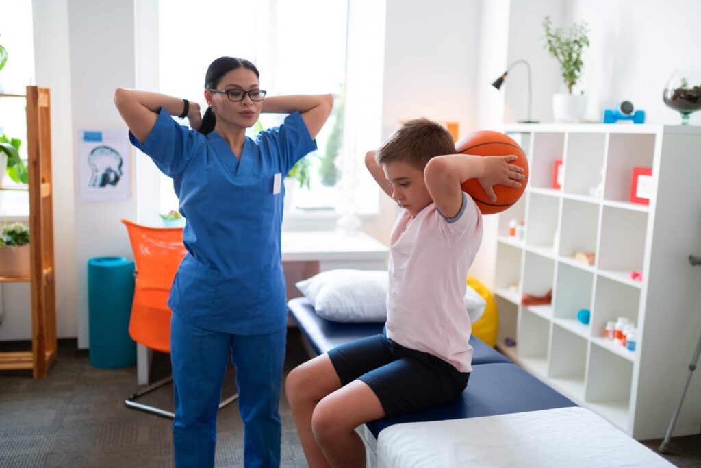 Physical therapist examining state of her patient while he is training with a ball