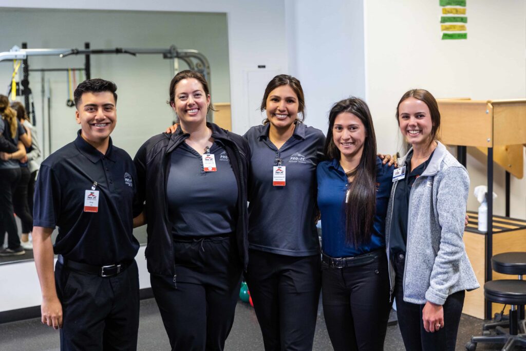 A team of Pro~PT physical therapists are smiling and standing together.