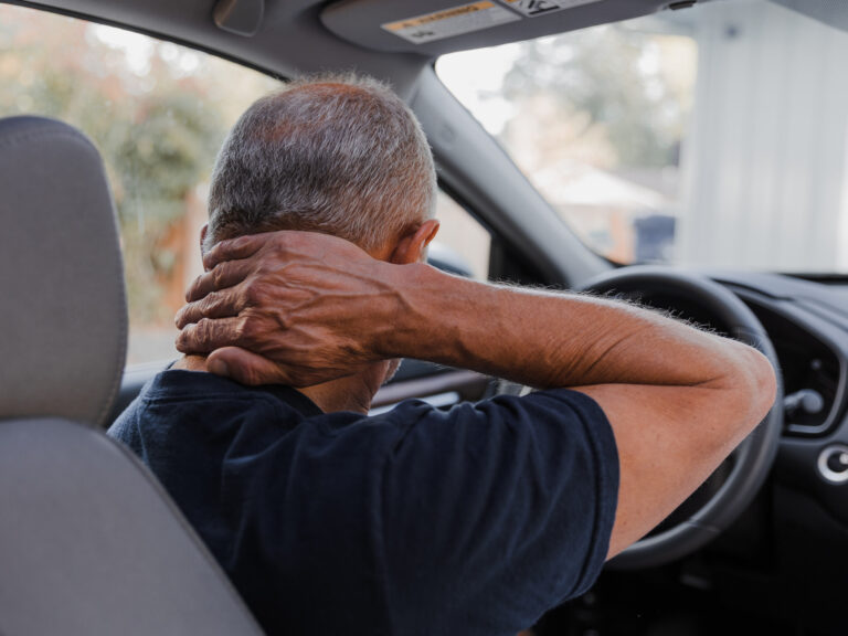 An older gentlemen wraps his left hand around his neck in pain.
