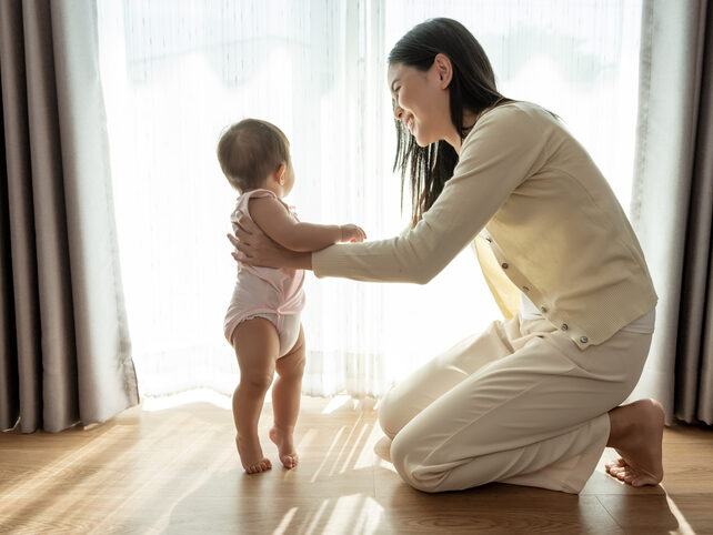 A baby girl learning first steps walk with mother, family, child, childhood and parenthood concept